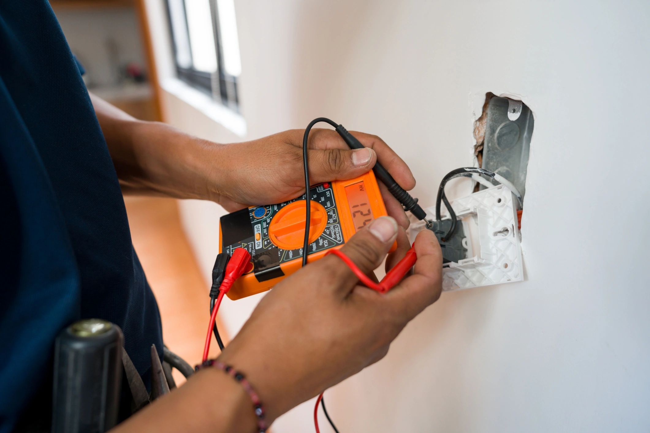 Person using a multimeter to test electrical wiring in a wall socket.