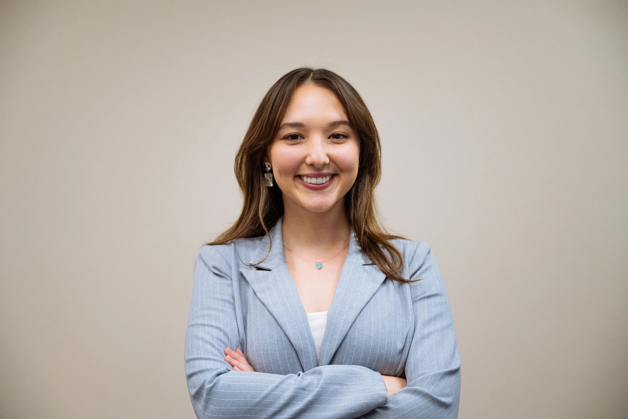 Confident young woman in a light blue blazer smiling with arms crossed.