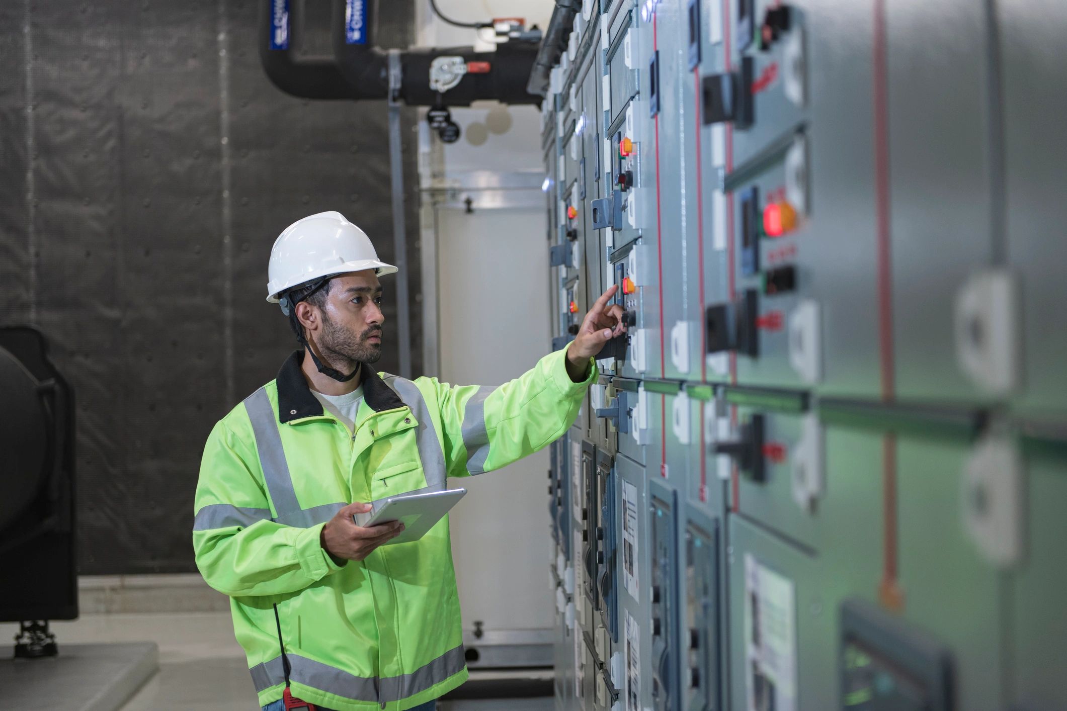 Engineer in safety gear inspecting electrical control panels.